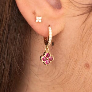 Peut inclure: Une créole dorée avec une breloque en forme de fleur à quatre pétales, ornée de quatre pierres rondes rose vif. L'anneau est serti d'une rangée de minuscules pierres blanches transparentes. Une petite puce d'oreille dorée avec une fleur blanche.