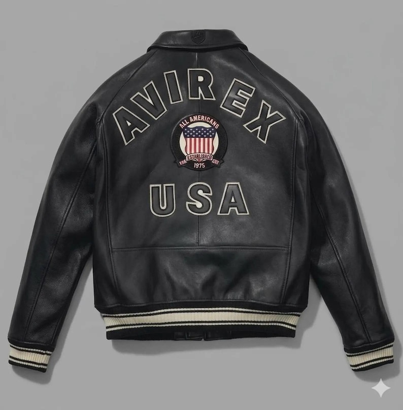 May include: A black leather jacket featuring the text AVIREX in white arched lettering across the upper back. Below the text is a circular patch with a United States flag and the words ALL AMERICANS ESTABLISHED 1975. The word USA is below the patch.
