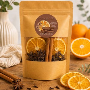May include: A brown kraft paper pouch containing dried orange slices, cinnamon sticks, star anise, and cloves. The circular label reads Cinnamon Harvest with a list of ingredients. The pouch has a clear window displaying the contents inside.