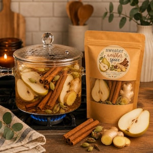 May include: A clear glass pot with a lid containing sliced pears, cinnamon sticks, ginger, and cardamom pods on a stove. Next to it is a brown paper pouch labeled sweater weather spice with a window showing the same ingredients inside.