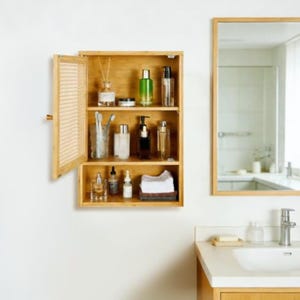 Könnte beinhalten: Ein an der Wand montierter Badezimmerschrank aus Holz mit offener Tür und einem Geflecht-Paneel. Das Innere verfügt über drei Regale mit verschiedenen Glasflaschen, einem Zahnbürstenhalter und einem Stapel gefalteter weißer Handtücher.