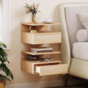 Peut inclure: Un ensemble de deux tables de chevet flottantes en bois clair fixées au mur. Chaque unité dispose d'une étagère ouverte et d'un tiroir coulissant. L'unité supérieure porte un vase doré avec des fleurs et une tasse blanche, celle du bas une montre.