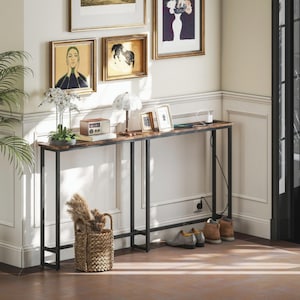 Può includere: Un tavolo console lungo e stretto con una superficie in venature di legno scuro e una struttura in metallo nero. Il tavolo include una ciabatta integrata con un cavo di ricarica bianco. Poggia su quattro gambe sottili con una barra di supporto.
