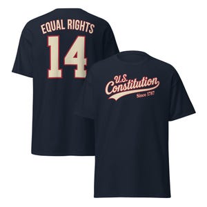 Puede incluir: Una camiseta azul marino con un gráfico frontal que dice U.S. Constitution Since 1787 en crema y rojo. La parte posterior de la camiseta muestra el texto Equal Rights sobre el número 14 grande en crema con un borde rojo, imitando una camiseta.