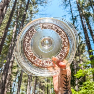 May include: A clear glass lid with a brown patterned design. The pattern features a variety of small images, including flowers, leaves, and geometric shapes.