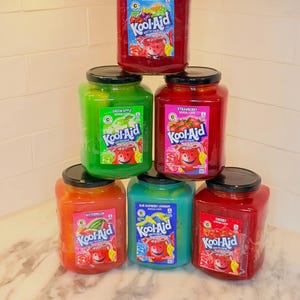 Peut inclure: Une pyramide de six bocaux en verre carrés remplis de préparation pour boisson Kool-Aid colorée. Les parfums incluent Tropical Punch, Green Apple, Strawberry, Watermelon, Blue Raspberry Lemonade et Cherry, avec couvercle noir et étiquette.