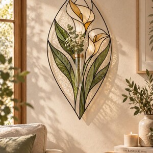 May include: A leaf-shaped wall art piece featuring a black metal frame with stained glass panels in shades of green, white, and yellow depicting calla lilies. A clear glass test tube vase is attached to the center, holding small green sprigs.