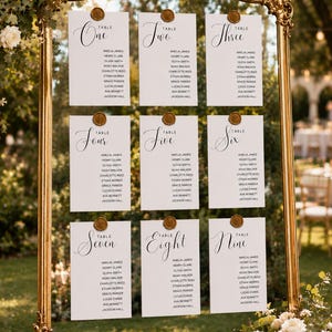 May include: A large, ornate gold-coloured frame holds nine white rectangular cards arranged in three rows. Each card features the word Table followed by a number from One to Nine in script, with a list of names below and a gold wax seal at the top.