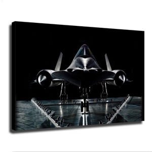 Op de afbeelding: Een vooraanzicht van een zwart SR-71 Blackbird vliegtuig op een reflecterende vloer. De jet heeft een scherpe, puntige neus, twee prominente motorgondels aan weerszijden en een landingsgestel dat zichtbaar is onder de romp.