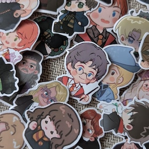 Può includere: Una collezione di adesivi in vinile fustellati con illustrazioni in stile chibi di vari personaggi della serie Harry Potter, tra cui figure con bacchette, uniformi scolastiche e creature magiche in una varietà di colori e pose.