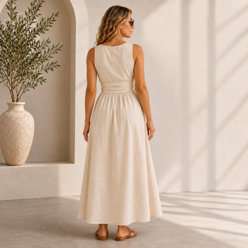 May include: A sleeveless, floor-length cream-colored dress with a fitted bodice, a defined waistline, and a full, flowing skirt. The dress features a simple round neckline and a clean, solid-colored design that reaches down to the ankles.