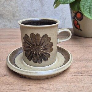 Peut inclure: Un ensemble tasse et soucoupe en céramique beige orné d'un motif floral marron foncé sur la tasse. L'intérieur de la tasse est marron foncé et la soucoupe présente un bord assorti. La céramique possède une finition mate et texturée.