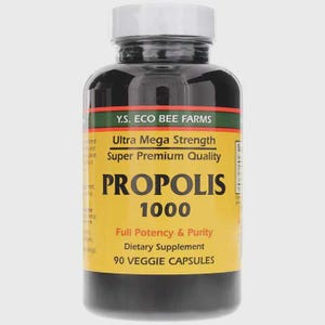 Puede incluir: Un frasco de plástico marrón oscuro con tapa de rosca blanca que contiene 90 cápsulas vegetales. La etiqueta amarilla presenta el texto Y.S. ECO BEE FARMS, Ultra Mega Strength, Super Premium Quality, PROPOLIS 1000, Full Potency & Purity y Dietary Supplement.