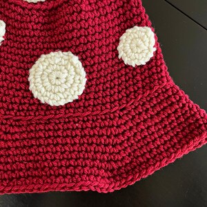 May include: A close-up of a red crocheted mushroom with white crocheted polka dots.