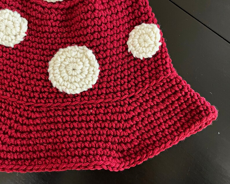 May include: A close-up of a red crocheted mushroom with white crocheted polka dots.