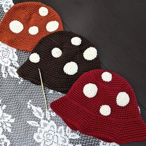 May include: Three crocheted hats in the shape of mushrooms. The hats are brown, red, and orange with white polka dots.