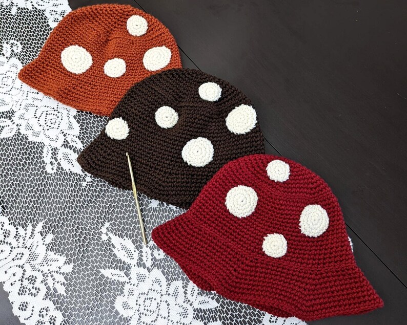 May include: Three crocheted hats in the shape of mushrooms. The hats are brown, red, and orange with white polka dots.