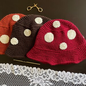 May include: Three crocheted hats in different colors: orange, brown, and red. Each hat has white polka dots and a wide brim.