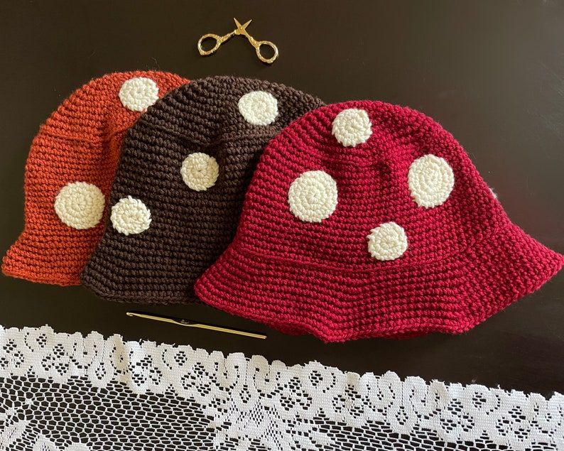 May include: Three crocheted hats in different colors: orange, brown, and red. Each hat has white polka dots and a wide brim.