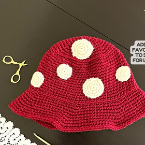May include: A red crocheted hat with white crocheted circles. The hat has a wide brim and is made with a textured stitch.