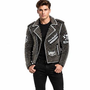 Puede incluir: Una chaqueta de moto de cuero negro densamente cubierta de tachuelas de metal plateado. La chaqueta presenta ribetes blancos, un bolsillo con cremallera con el texto DISCHARGE, un parche de calavera y caracteres japoneses en la manga izquierda.