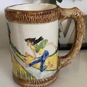 May include: A ceramic mug with a brown handle and a white body. The mug features a colorful illustration of a person running on a path with a yellow background. The mug is signed "Carol Wells".