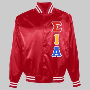 May include: A red satin varsity jacket featuring a snap-button front closure, long sleeves, and ribbed cuffs and hem with white stripes. The front displays the Greek letters Sigma, Iota, and Alpha vertically in red, yellow, and blue colours.