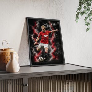 Könnte beinhalten: Ein gerahmter, rechteckiger Kunstdruck für die Wand, der einen Fußballspieler in rotem Trikot und weißer Hose zeigt, wie er einen Fußball tritt. Der Spieler ist von dynamischen rot-weißen Raucheffekten vor einem dunklen Stadionhintergrund umgeben.