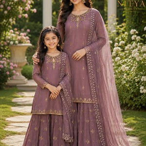 May include: Two matching mauve-colored outfits consisting of a long-sleeved tunic with a keyhole neckline and a flared skirt, both featuring gold embroidery and sequins. Each set includes a sheer, matching mauve dupatta with gold trim.
