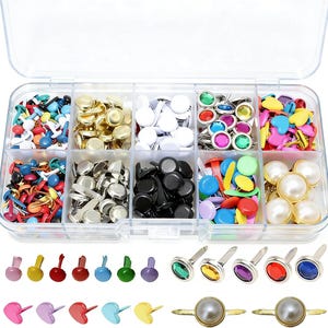 May include: A clear plastic storage container with ten compartments filled with various metal brads, including solid colors, metallic finishes, heart shapes, faux pearls, and colorful gemstone-style tops, with loose samples displayed below.
