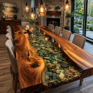 May include: A long dining table featuring a live-edge wood slab on each side with a central glass-topped channel filled with smooth, multi-colored river stones. The table is surrounded by eight upholstered chairs in a light gray fabric.