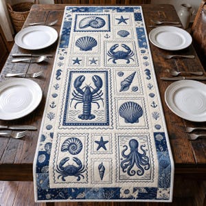 May include: A rectangular quilted table runner featuring a cream-coloured background with a repeating pattern of blue nautical illustrations. The design includes a lobster, octopus, crabs, starfish, and various seashells framed in postage stamp borders.