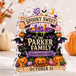 May include: A clear acrylic plaque featuring a black cauldron filled with purple liquid, surrounded by pumpkins, a black cat, and sweets. The text reads SPOOKY SWEET, THE PARKER FAMILY, HALLOWEEN 2026, and OCTOBER 31, decorated with ghosts, bats, and colourful treats.