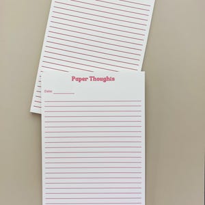 May include: Two white rectangular notepad sheets with red horizontal lines and the text Paper Thoughts printed at the top. Each sheet features a red Date line in the upper left corner. The sheets are stacked slightly offset from one another.