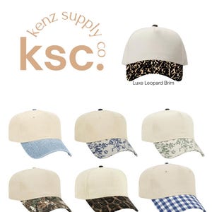 May include: A collection of seven baseball caps with cream-colored crowns and varied brims, including leopard print, blue denim, blue floral, green floral, camouflage, cheetah print, and blue gingham patterns, with the text kenz supply co ksc.