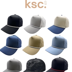 May include: A collection of nine baseball caps with a kenz supply co. ksc logo at the top. The caps feature various solid colors including black, gray, tan, and blue, with some designs incorporating mesh back panels and a decorative rope trim.