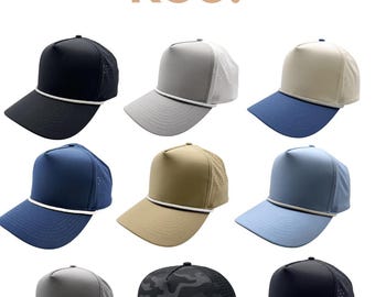 May include: A collection of nine baseball caps with a kenz supply co. ksc logo at the top. The caps feature various solid colours including black, grey, tan, and blue, with some designs incorporating mesh back panels and a decorative rope trim.