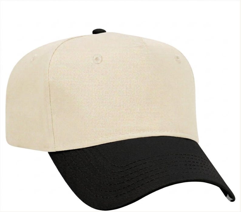 May include: A baseball cap featuring a solid cream-coloured crown and a contrasting black visor. The cap has a structured front panel, a small black button at the top centre, and visible stitching along the curved brim, providing a clean look.