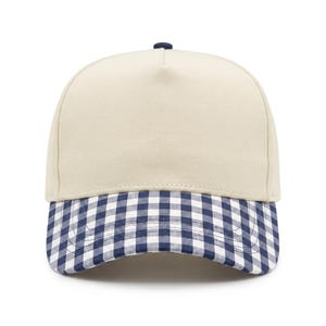 May include: A five-panel baseball cap featuring a solid cream-colored crown and a navy blue and white gingham checkered brim. The cap includes a small navy blue button at the top center, structured front panels, and a curved visor design.