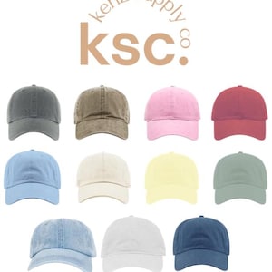 May include: A collection of eleven baseball caps in various solid colors including gray, brown, pink, red, light blue, cream, yellow, sage green, light denim blue, white, and navy blue, arranged under the text kenz supply co ksc.
