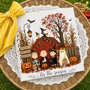 Op de afbeelding: Een vierkante canvasprint met Peanuts-personages in Halloween-kostuums voor een rood hondenhok. De scène bevat pompoenen, een bord voor een maïsdoolhof en een boom met herfstbladeren. De tekst onderaan luidt 'Tis the season'.