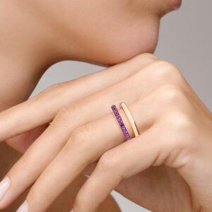 Könnte beinhalten: Ein Set aus zwei Ringen an einem Finger. Ein Ring ist ein schlichter, polierter Goldring mit einer glatten, abgerundeten Oberfläche. Der zweite Ring ist ein dünner Goldring mit einer durchgehenden Reihe kleiner, leuchtend pinker Edelsteine.