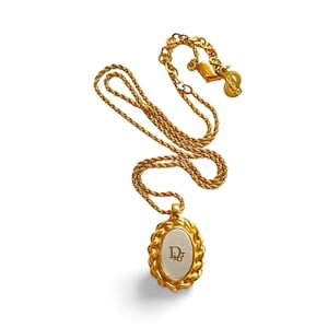 May include: Gold-toned necklace with an oval pendant featuring the letters "D" and "r" in a serif font. The pendant is framed by a rope-like border. The chain and clasp are also gold-toned.
