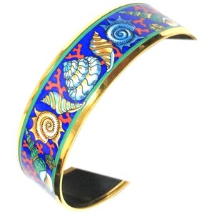 May include: A gold-toned cuff bracelet featuring a vibrant blue enamel surface decorated with a pattern of various seashells in shades of white, yellow, and green, interspersed with bright red coral-like branches and a thin green border.