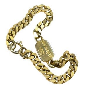 K&ouml;nnte beinhalten: Ein goldfarbenes Panzerkettenarmband mit einem rechteckigen Anh&auml;nger. Der Anh&auml;nger tr&auml;gt das Wort "Valentino" und ein eingraviertes Logo. Das Armband besteht aus ineinandergreifenden ovalen Gliedern und hat einen Verschluss.