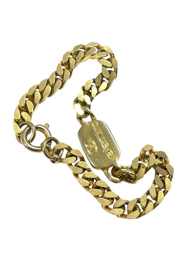 K&ouml;nnte beinhalten: Ein goldfarbenes Panzerkettenarmband mit einem rechteckigen Anh&auml;nger. Der Anh&auml;nger tr&auml;gt das Wort "Valentino" und ein eingraviertes Logo. Das Armband besteht aus ineinandergreifenden ovalen Gliedern und hat einen Verschluss.