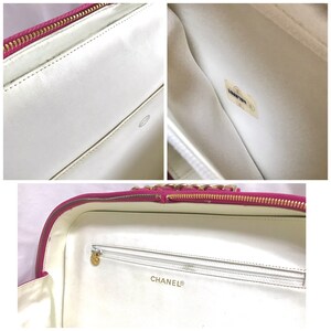 May include: A white leather Chanel makeup bag with a pink zipper and gold chain detail. The bag has a white lining with a zippered pocket and the Chanel logo.