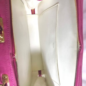 May include: The inside of a pink fabric handbag with a white lining and a zipper closure. The bag has a small pocket on the inside.