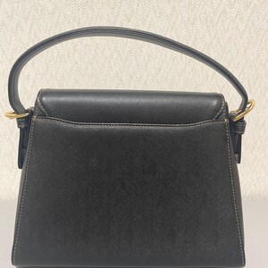 Puede incluir: Bolso de mano negro con asa curva y herrajes dorados. El bolso tiene forma rectangular con cierre de solapa y costuras visibles. El asa est&aacute; sujeta al bolso con aros dorados.