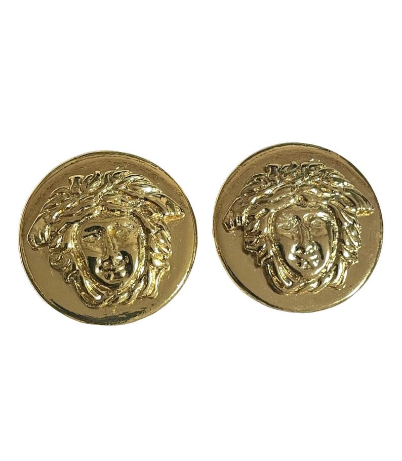 May include: A pair of gold-tone earrings featuring a raised, detailed design of a Medusa head.